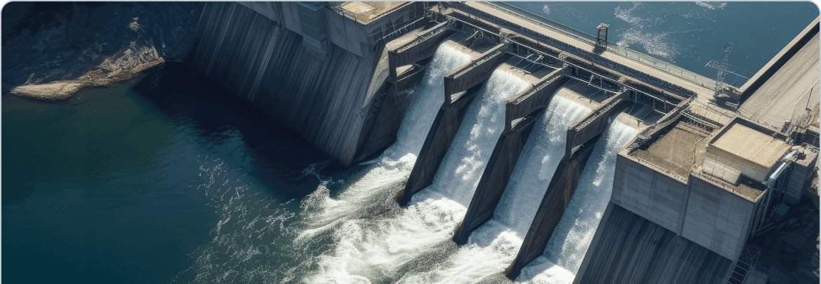 Aerial view of a large concrete dam with multiple open floodgates releasing powerful white water into a blue-green river below.